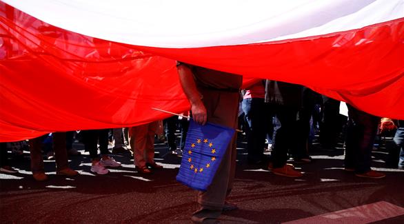 رجل يحمل علم الاتحاد الأوروبي تحت العلم البولندي خلال مظاهرة معارضة للحكومة في وارسو (رويترز)