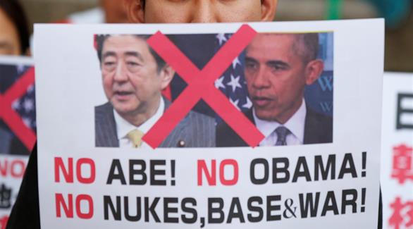 متظاهر ياباني يحمل لافتة للاحتجاج ضد الرئيس الأمريكي أوباما والوزراء الياباني شينزو آبي، في حديقة السلام التذكارية في هيروشيما(رويترز)
