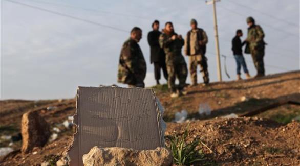 مقاتلون أكراد أمام  لافتة كرتونية كتب تحذر من السير فوق المدفن الجماعي (أ ب)