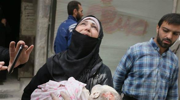 امرأة تحمل جثة طفلة بين يديها وسط أنقاض المباني في سوريا (الئتلاف السوري)