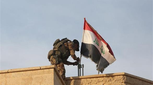 أحد عناصر الجيش العراقي يرفع العلم العراقي فوق أحد المباني(المصدر)
