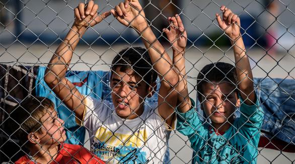 أطفال سوريون يقفون وراء سياج بمخيم للاجئين في منطقة كيليس جنوب شرق تركيا (أ ف ب)