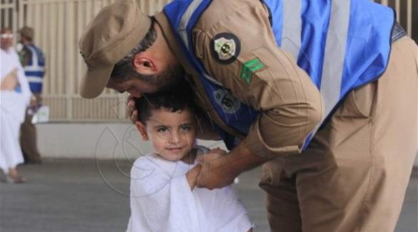 رجل أمن يداعب طفلاً يرتدي ثياب الإحرام في منى (صحيفة الشرق)