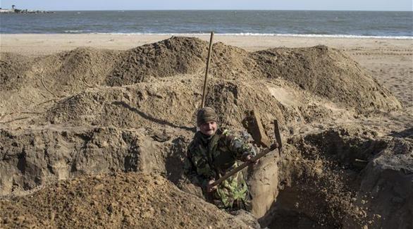 جندي أوكراني يحفر خندق على الشاطئ بحر آزوف بميناء مدينة ماريوبول (رويترز)