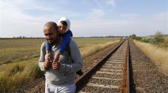 لاجئ سوري يحمل ابنه المصاب بعدما تجاوزا الحدود بين صربيا والمجر(أرشيف)