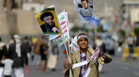 بائع يتجول حاملاً صور الحوثي ونصرالله وشعارات الإنقلابيين (رويترز)
