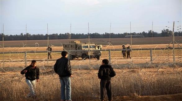 شباب فلسطينيون  في غزة يراقبون جنوداً إسرائيليين على الجانب الآخر من السياج (أرشيف)