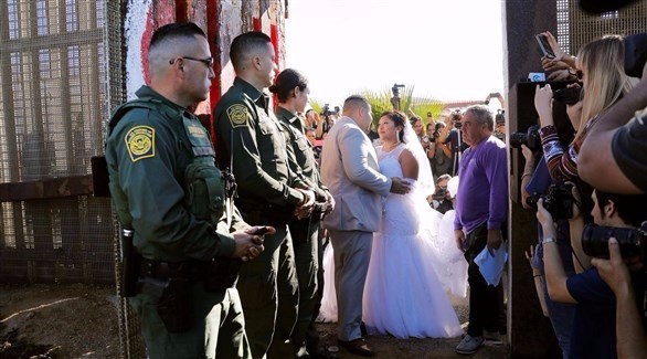 العروس إيفيليا رييس مع عريسها أمام الجدار الفاصل بين أمريكا والمكسيك (المصدر)
