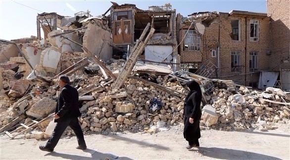 إيرانيان يمران بالقرب من منازل مدمرة بفعل الزلزال الأخير (اي بي ايه)