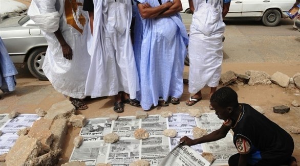 أشخاص يقفون بجانب صبي ينشر الصحف في موريتانيا (أرشيف / غيتي)