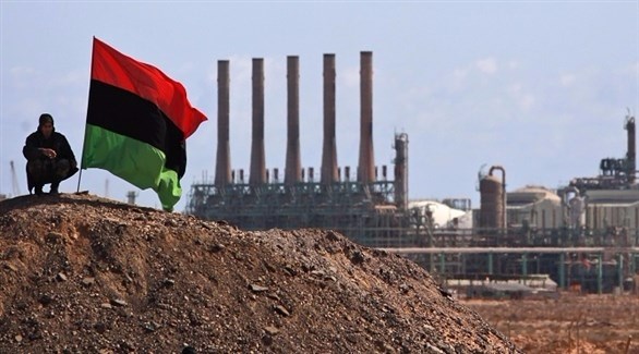 رجل يقف بالقرب من العلم الليبي ويظهر خلفه منشأة نفطية (أرشيف)