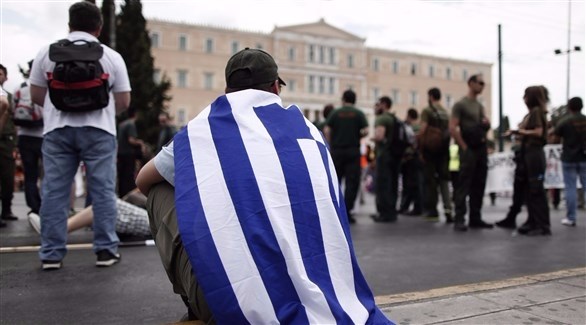 عنصر من شرطة البلدية في اليونان يلتف بالعلم اليوناني خارج أسوار البرلمان في أثينا (أرشيف  / أ ب)