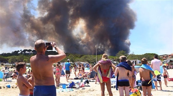 سواح على احد الشواطئ لفرنسية يلتقطون صوراً للحريق (أ ف ب)