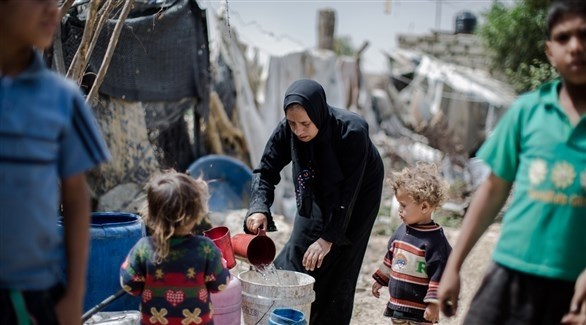 سيدة تملأ الماء تحت أنظار طفلين في غزة (أرشيف)