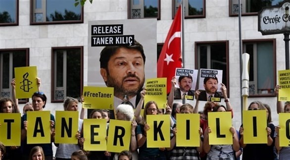 متظاهرون يحملون صور تانير كيليتش بجانب العلم التركي (أمنظمة العفو الدولية)