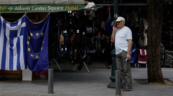 رجل يمر بجانب علمي الاتحاد الأوروبي واليوناني (رويترز)