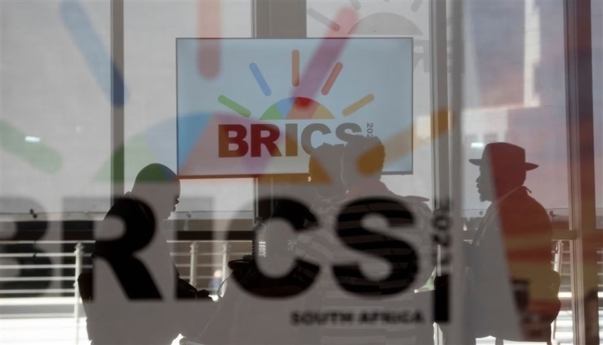 مندوبو جنوب إفريقيا يجلسون خلف زجاج عليه شعار البريكس أثناء انعقاد قمة البريكس في جوهانسبرغ (رويترز)