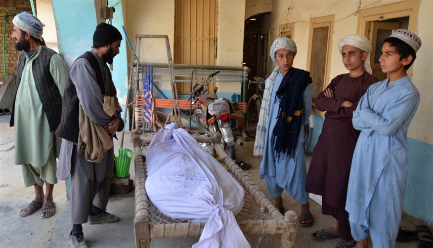 أشخاص يقفون أمام جثة شخص قتل بانفجار قندهار في جنوب أفغانستان (أ ف ب)
