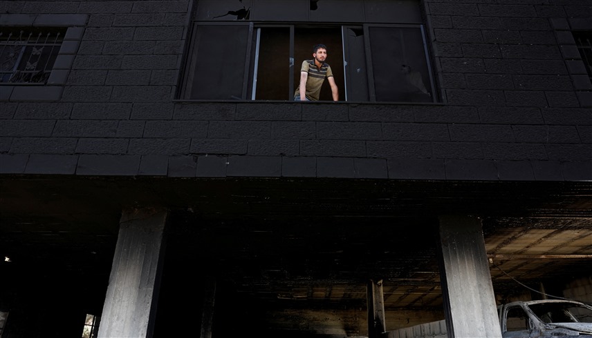 فلسطيني ينظر من نافذة منزله المتفحم (وكالات)