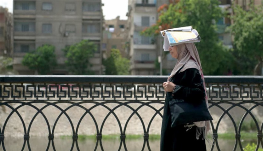 سيدة مصرية تضع كتاباً فوق رأسها لحمايتها من أشعة الشمس (رويترز)