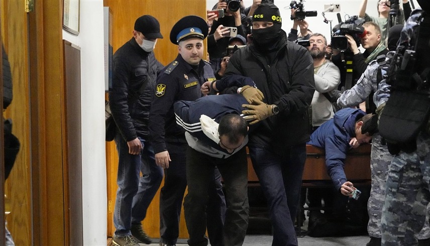 عنصر أمن روسي يقتاد متهماً بالتورط في الهجوم على قاعة كروكوس في موسكو (أرشيف)