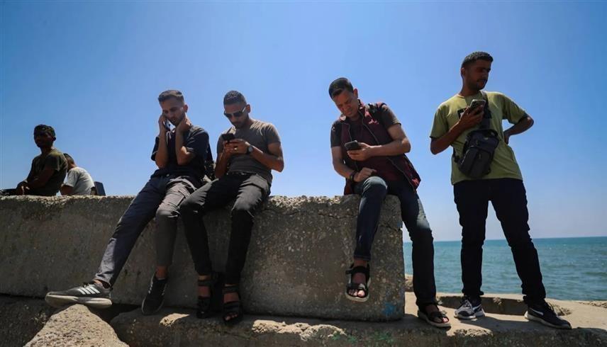 فلسطينيون يحاولون التقاط إشارة الانترنت قرب شاطئ البحر (رويترز)
