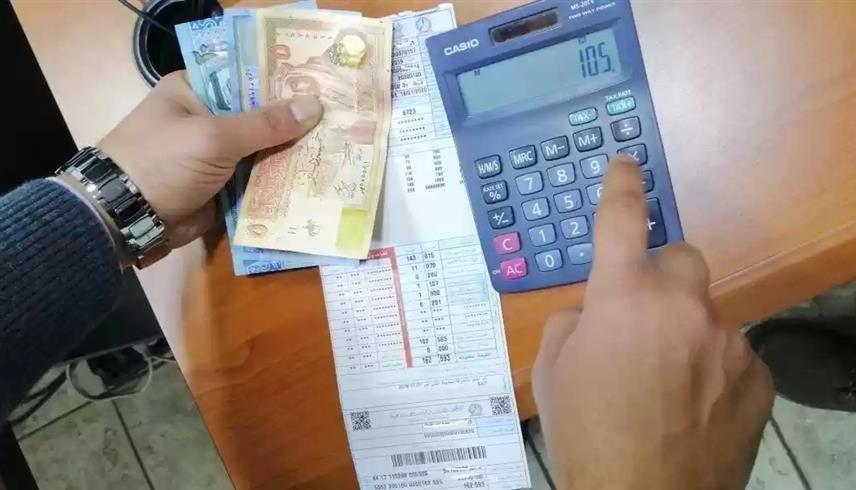 شخص يمسك بآلة حاسبة ونقود وفاتورة كهرباء في الأردن (وسائل التواصل الاجتماعي)