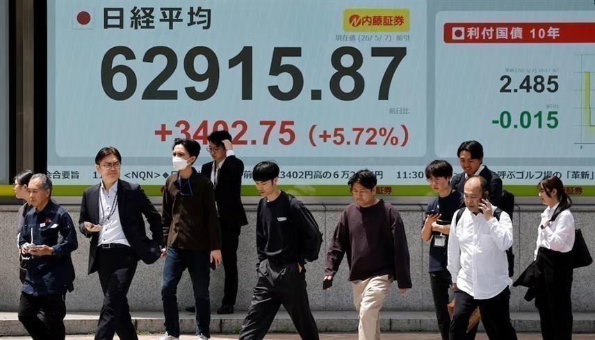 مشاة يسيرون أمام لوحة إلكترونية تعرض أسعار الأسهم وحركة تداولها على المؤشر نيكي الياباني خارج إحدى شركات الوساطة المالية في طوكيو (رويترز)