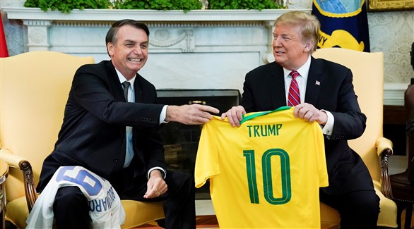 ترامب وبولسونارو خلال تبادل قمصان منتخبي أمريكا والبرازيل (رويترز)