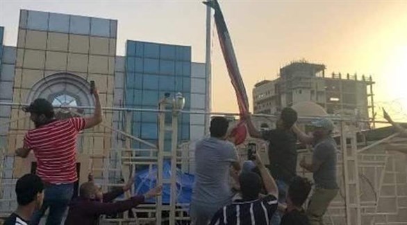 عراقيون ينزلون العلم الكويتي عن سارية أمام  القنصلية في البصرة (تويتر)