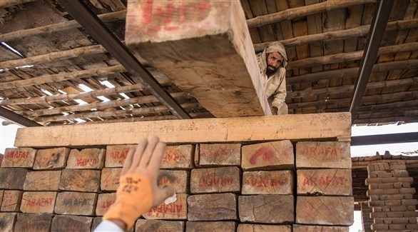 عمال يكدسون قطع الخشب المنقولة من كونار، في مستودع في جلال أباد.(أرشيف)