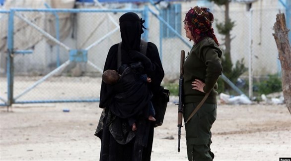 زوجة أحد مقاتلي داعش تقف إلى جانب مقاتلة من قسد في مخيم الهول (أرشيف)
