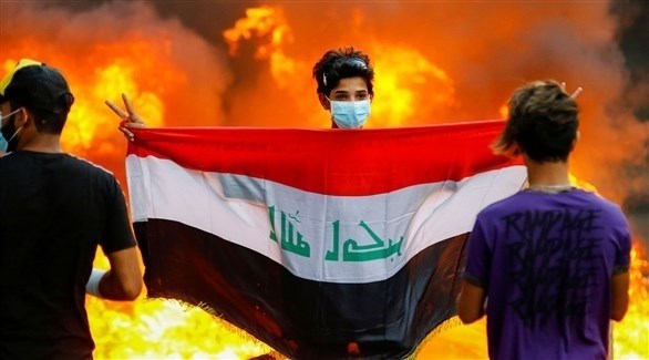 محتج عراقي شاب يرفع علم بلاده وإشارة النصر في بغداد (إ ب ا)