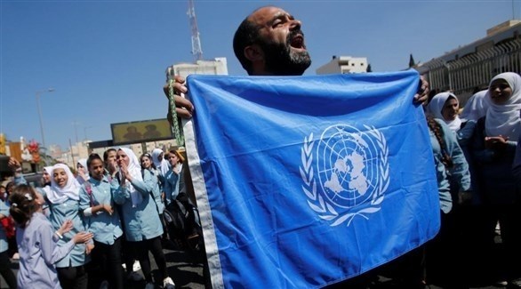 رجل يحمل علم الأمم المتحدة بجانب أحد مباني الأونروا (أرشيف)