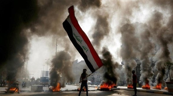 متظاهر يحمل العلم العراقي وسط الإطارات المحترقة (أرشيف)