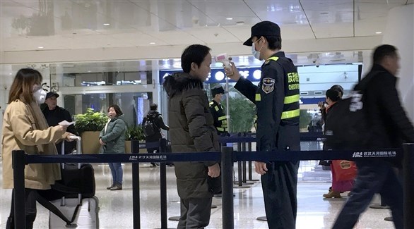 عنصر أمن صيني يفحص مسافرين في مطار ووهان الدولي (أ ب)