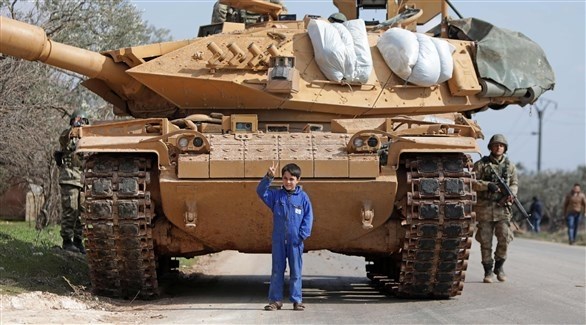 طفل سوري يقف قبالة دبابة تركية في إطار منطقة إدلب السورية (أ ف ب)