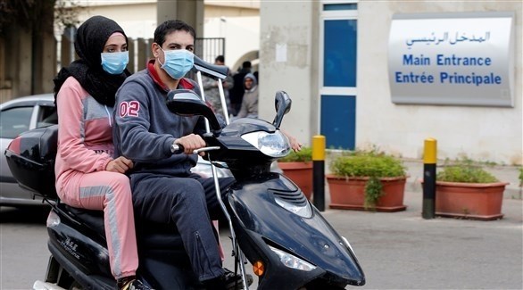 ركاب دراجة نارية يرتدون كمامات أمام مدخل مستشفى الحريري الحكومي (رويترز)