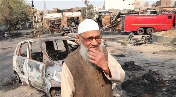 هندي وسط سيارة محترقة ومبانٍ مهدمة بسبب الاشتباكات (اي بي ايه)