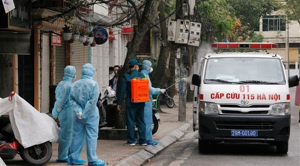 عمال يعقمون سيارة إسعاف قرب منزل مصاب بكورونا في هانوي (رويترز)