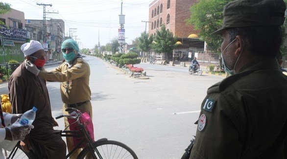 شرطي باكستاني يساعد رجلاً على وضع كمامة واقية في مولتان (إ ب أ)