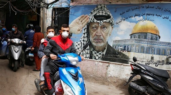 فلسطينيون في مخيم لاجئين أمام جدارية بصورة للزعيم الراحل ياسر عرفات (رويترز)