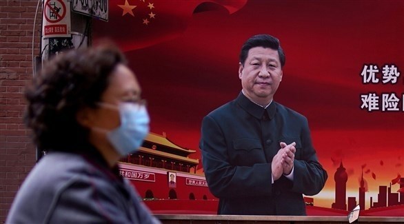 امرأة ترتدي كمامة أثناء مرورها بجانب صورة عملاقة للرئيس الصيني (أرشيف / رويترز)