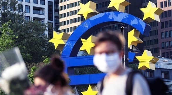 أشخاص يرتدون الكمامات أثناء مرورهم بجانب مجسم لعملة اليورو (أرشيف / غيتي)