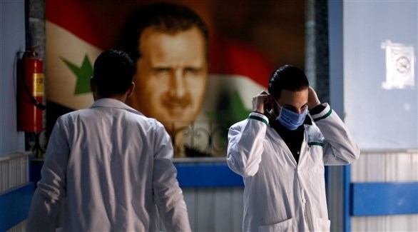 شخص يرتدي الكمامة وبانت صورة الرئيس السوري في الخلفية (أرشيف)