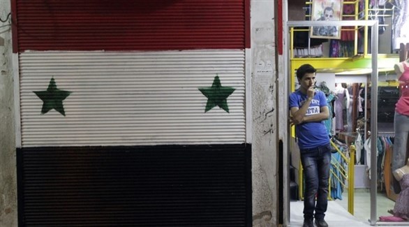 شخص يقف قبالة العلم السوري المرسوم على واجهة أحد المحال التجارية (أرشيف)