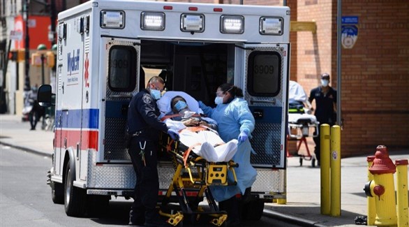 مسعفان ينقلان مصاباً بكورونا إلى سيارة إسعاف في نيويورك (أرشيف)