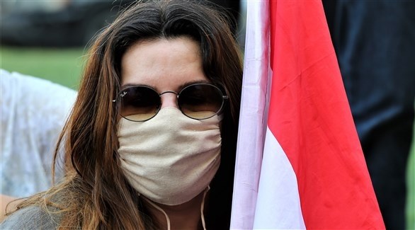 امرأة ترتدي كمامة وتحمل العلم اللبناني خلال إحدى التظاهرات في بيروت (اي بي ايه)