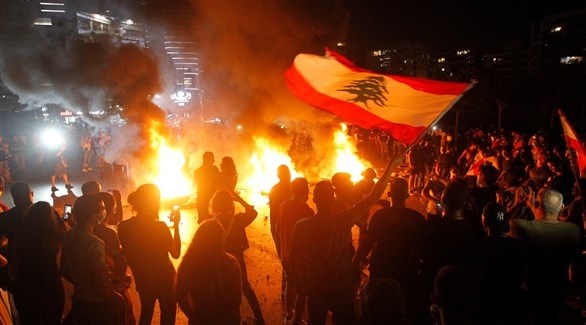 متظاهرون يرفعون العلم اللبناني بالقرب من النيران شمالي بيروت ( اي بي ايه)