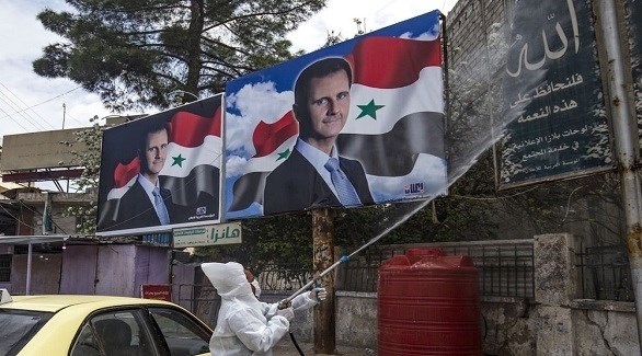 عامل في سوريا يعقم جداراً عليه صور الرئيس بشار الأسد (أرشيف)